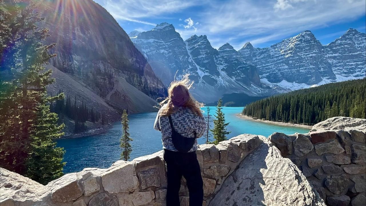 En kvinna st&aring;r p&aring; en klippv&auml;gg med utsikt &ouml;ver en sj&ouml;.