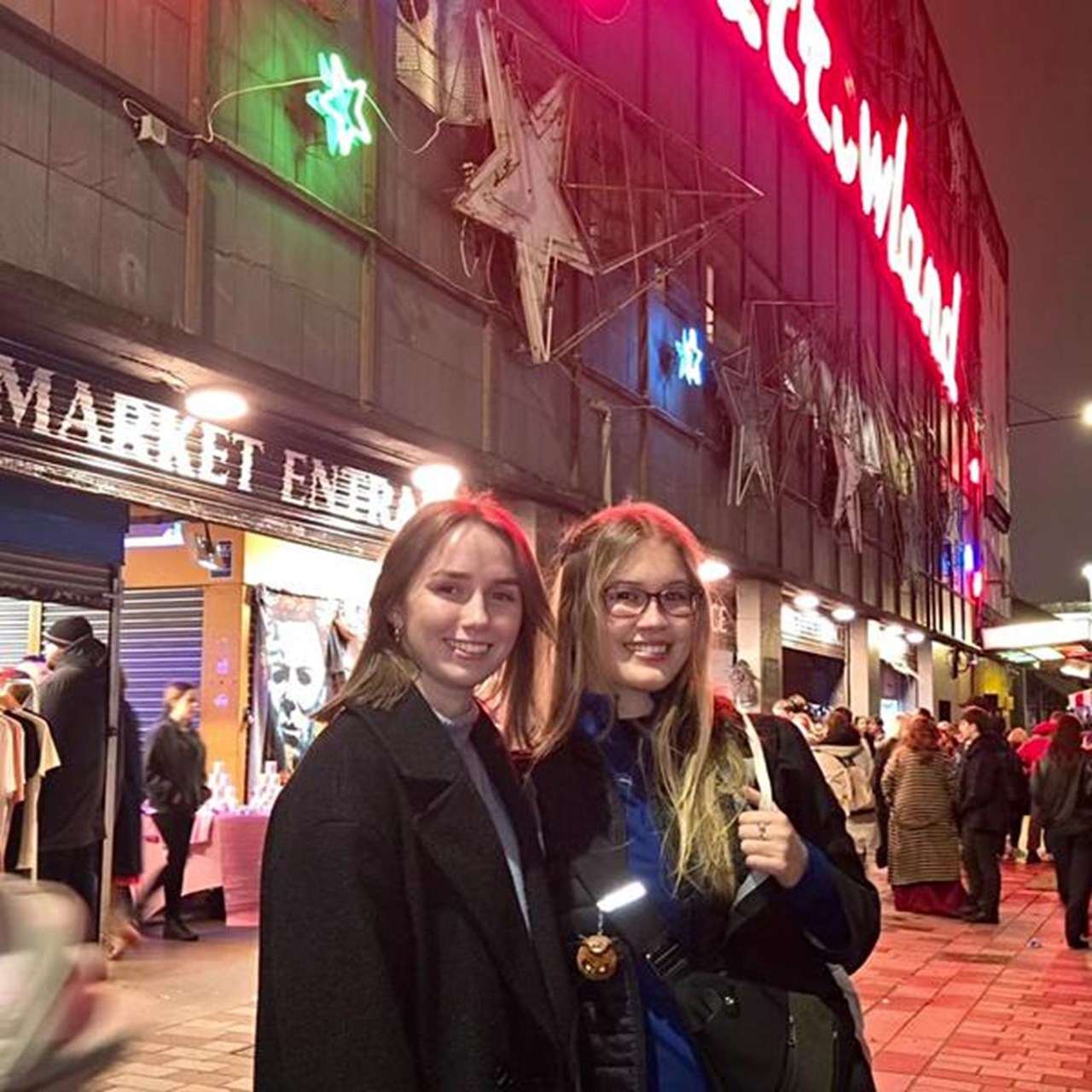 Tv&aring; kvinnor st&aring;r framf&ouml;r en butik p&aring; kv&auml;llen.