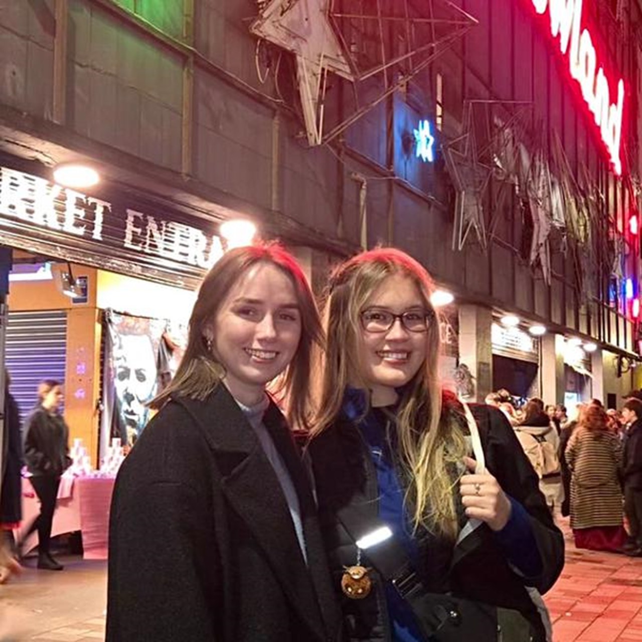 Två kvinnor står framför en butik på kvällen.