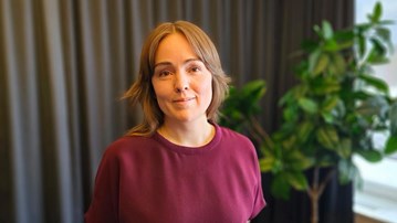 Porträtt av kvinna med mellanmörkt hår och lila tröja.