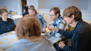 Fem personer sitter runt ett bord och samarbetar.