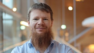 Alexandre Bartel i kort hår och skägg, står vid fönstret i ljusblå skjorta
