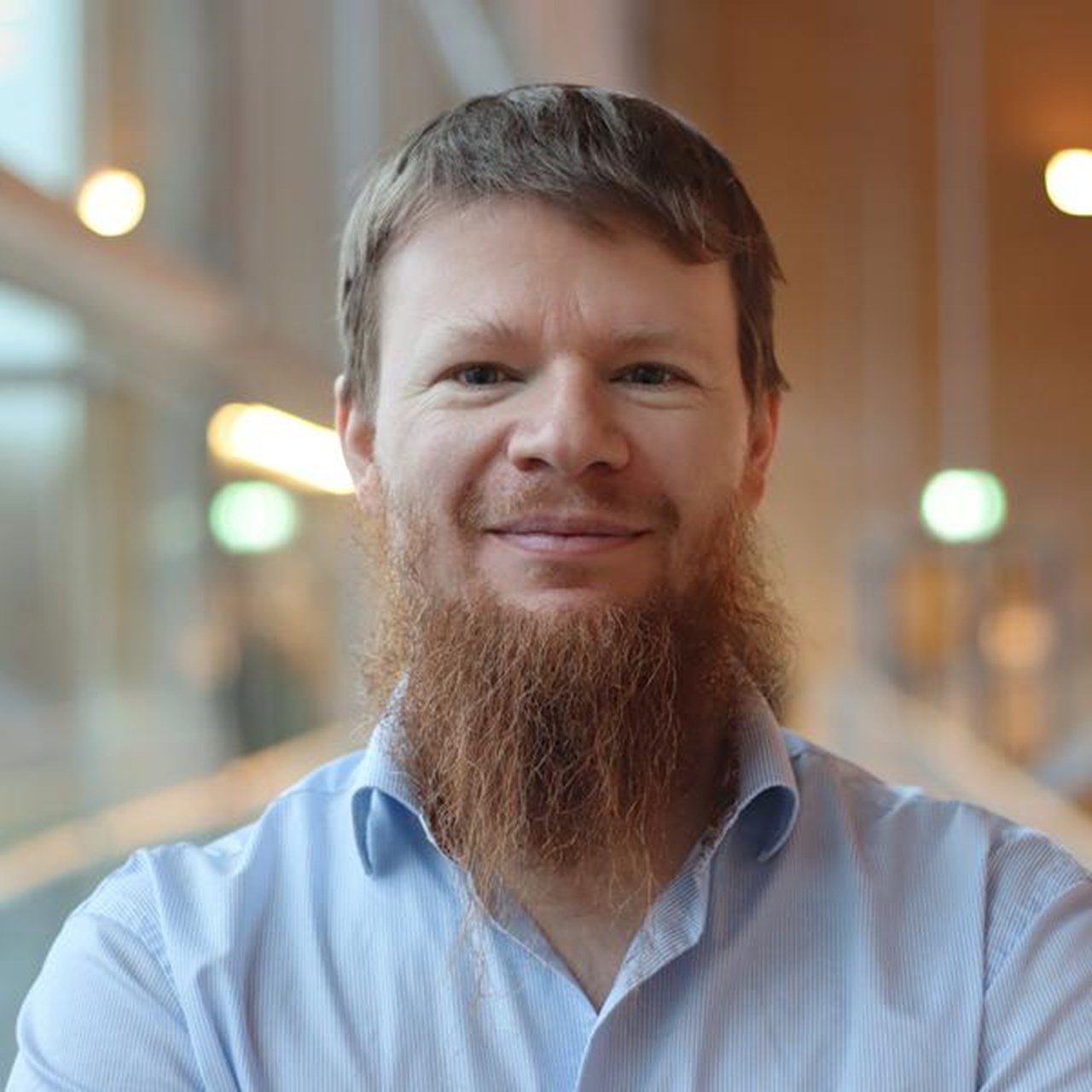 Alexandre Bartel i kort hår och skägg, står vid fönstret i ljusblå skjorta