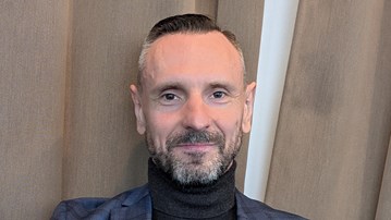 En man i blå kostym sitter framför en gardin.