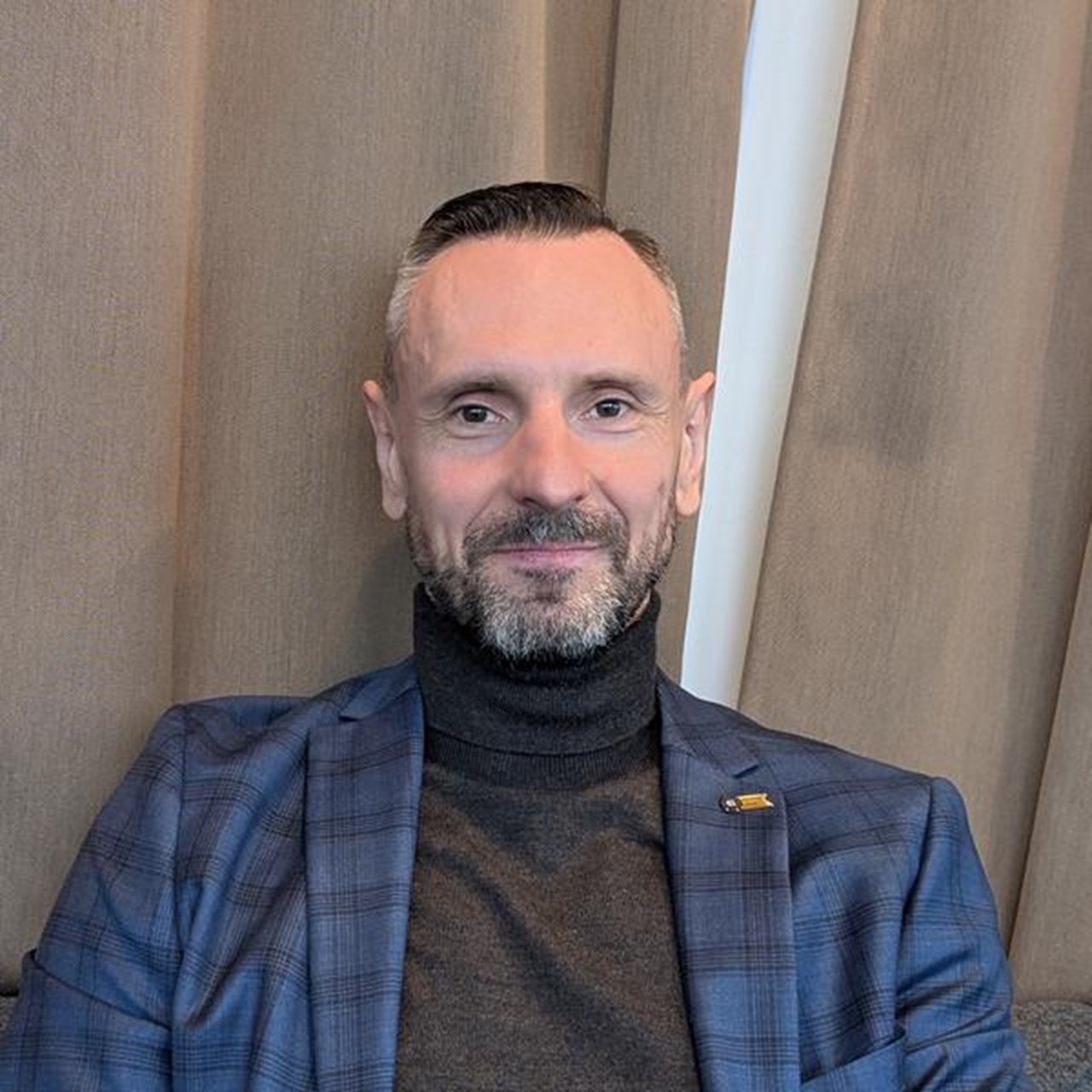 En man i bl&aring; kostym sitter framf&ouml;r en gardin.