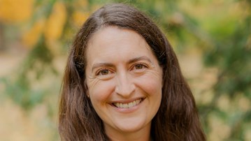 En kvinna med långt brunt hår som ler mot kameran.