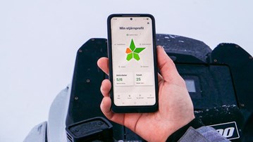 Person ute i vinterlandskap håller upp mobiltelefon med appen Star-C
