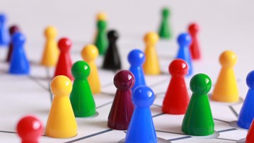 Olikfärgade spelpjäser i plast placerade på ett underlag med markeringar för att illustrera nätverk.