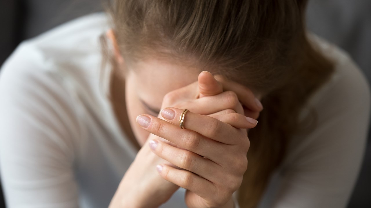 Kvinna som inte mår bra sitter lutad framåt med händerna knäppta framför ansiktet.