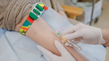 Närbild på ett armveck där ett blodprov just ska tas med hjälp av en kanyl på ett vakuumprovrör.