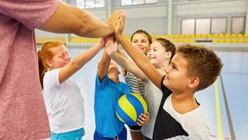 Barn i idrottshall som gör high five med varandra och en vuxen person. 