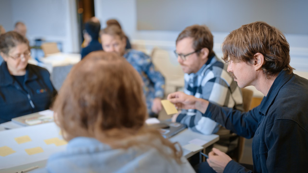Fem personer sitter runt ett bord och samarbetar.