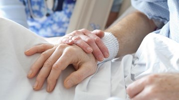 En person som håller en annan person i handen i en sjukhussäng.