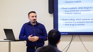 Cemal Erdem stands in front of a screen with a slide displayed describing his current research