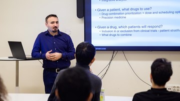Cemal Erdem stands in front of a screen with a slide displayed describing his current research
