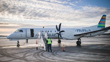 Ett flygplan som står på landningsplattan på Umeå flygplats. En flygplatsanställd håller på att ansluta trappan för att passagerare ska kunna gå ur planet.