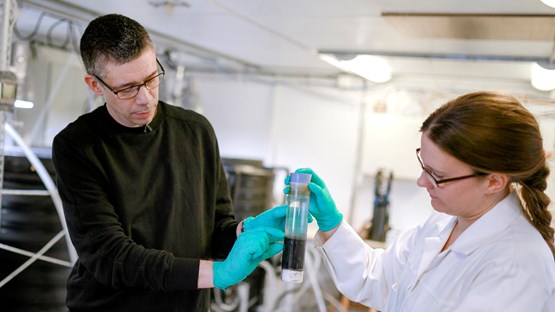 En man och en kvinna håller i ett större provrör med sediment i ett laboratorium.