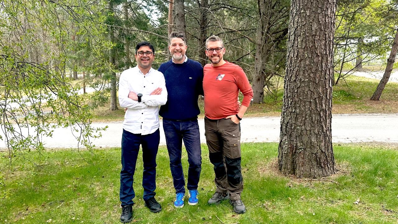 Three men are standing outdoors and posing for a group photograph./Tre m&auml;n st&aring;r utomhus och poserar f&ouml;r ett gruppfoto.