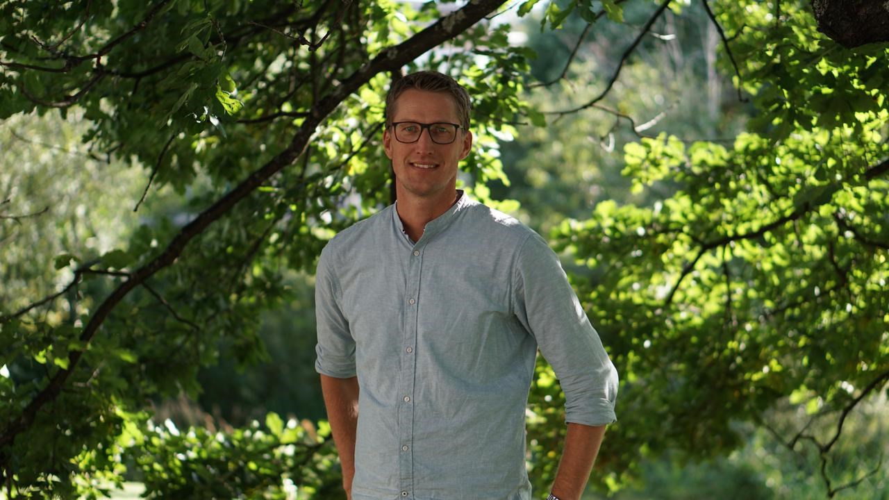 En man som st&aring;r under ett tr&auml;d med h&auml;nderna i fickorna.