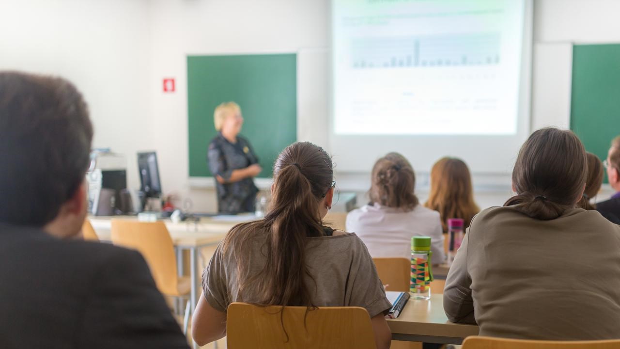 Föreläsningssal på universitet med studenter i förgrunden och en lärare vid tavlan.