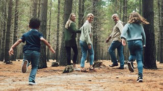 Familj med barn ute på promenad i barrskog.