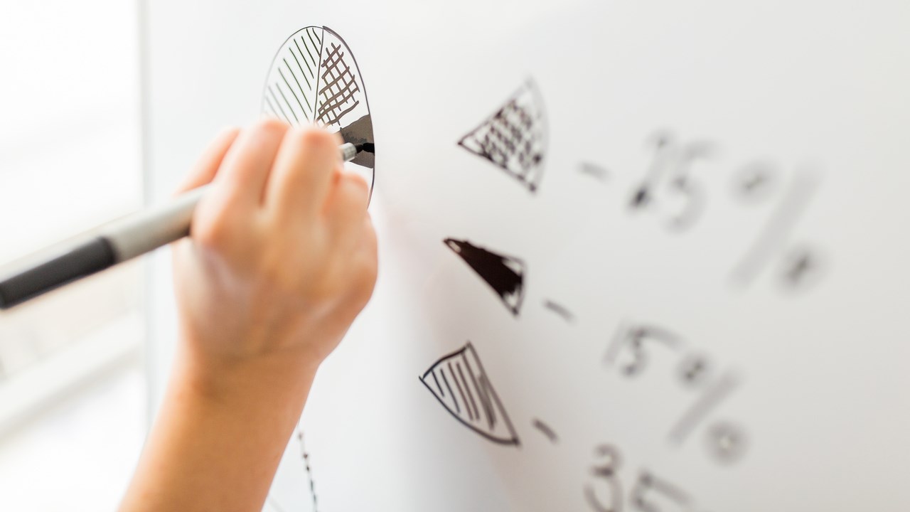 Närbild på hand som ritar diagram på whitboard-tavla.