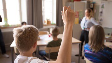 Mellanstadiebarn i klassrum. Pojke räcker upp handen.