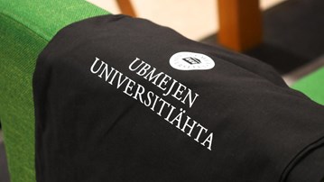 En svart tygpåse med texten Ubmejen universitiähta ligger på en grön soffrygg.