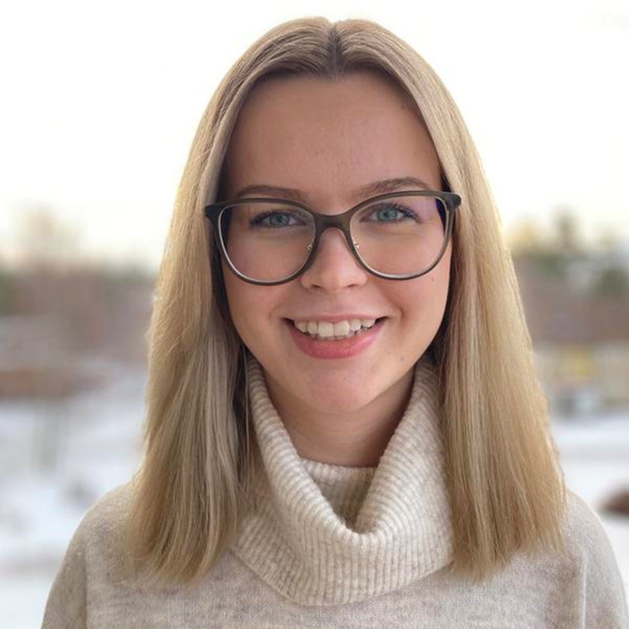 En kvinna med glas&ouml;gon som st&aring;r framf&ouml;r ett f&ouml;nster.