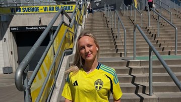 En kvinna i landslagströja står på en trappa.