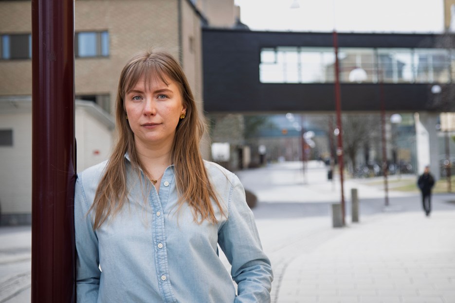 En kvinna som står lutad mot en stolpe på en trottoar.