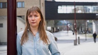 En kvinna som står lutad mot en stolpe på en trottoar.
