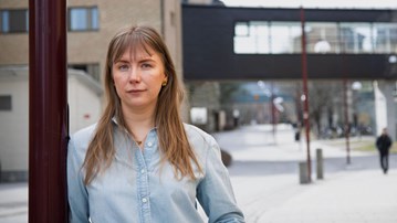 En kvinna som står lutad mot en stolpe på en trottoar.