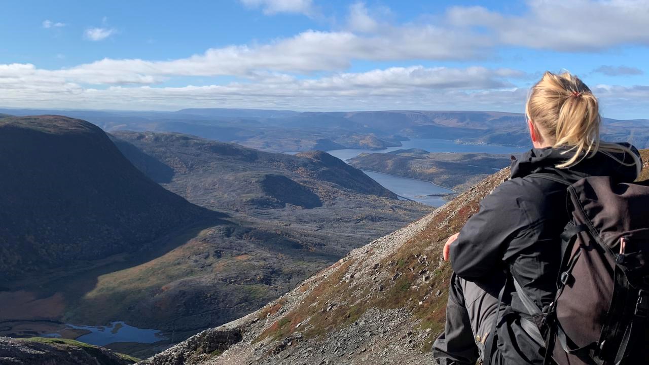 En vandrare med stor ryggsäck sitter på en höjd, med ryggen vänd mot kameran och blickar ut över landskapet.