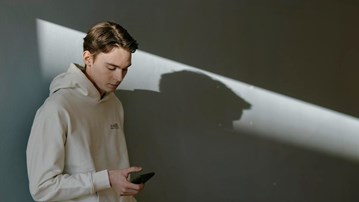 En man sitter vid ett bord med laptop och headset, böcker och antecknar i ett block.