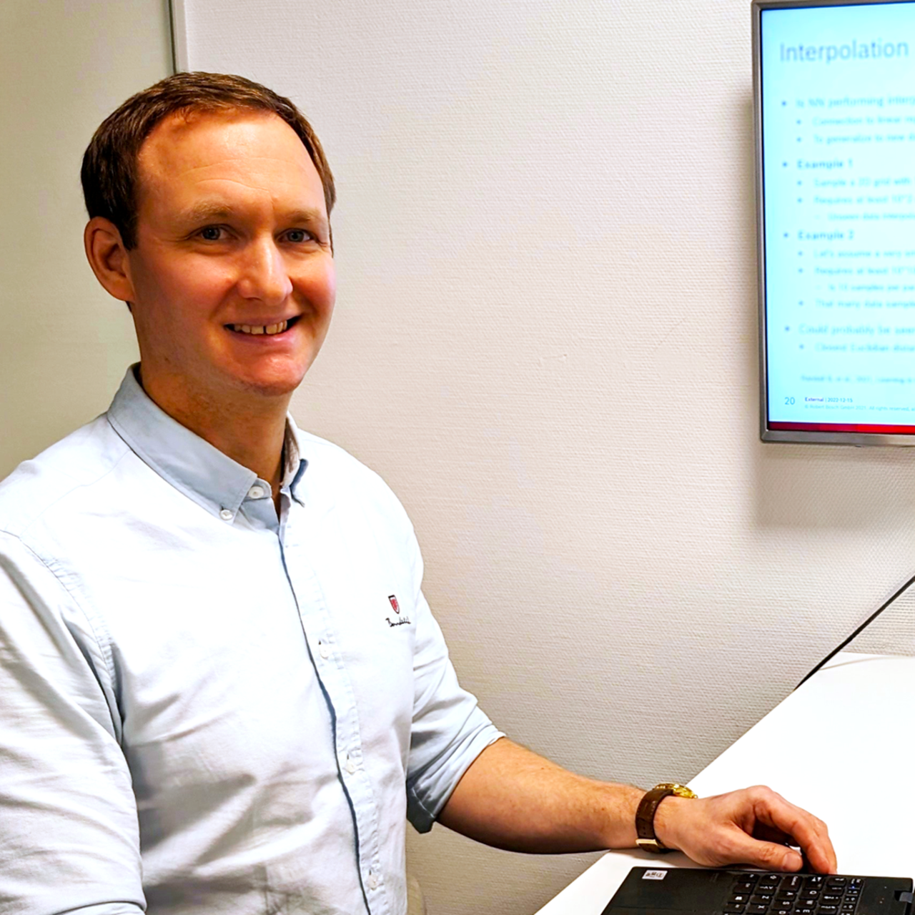 Thomas Nilsson sitter vid en bärbar  dator uppkopplad mot en större skärm. Han bär en ljusblå skjorta med uppkavlade ärmar