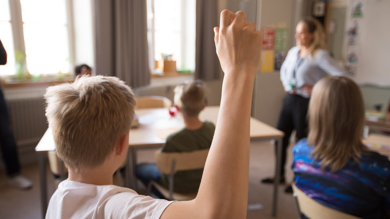 Mellanstadiebarn i klassrum. Pojke räcker upp handen.