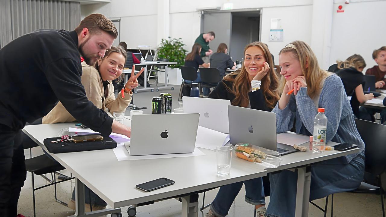 En man och tre kvinnor som arbetar tillsammans vid ett bort. P&aring; bordetsyns datorer.