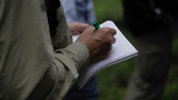 Närbild på händer som antecknar i ett kollegieblock