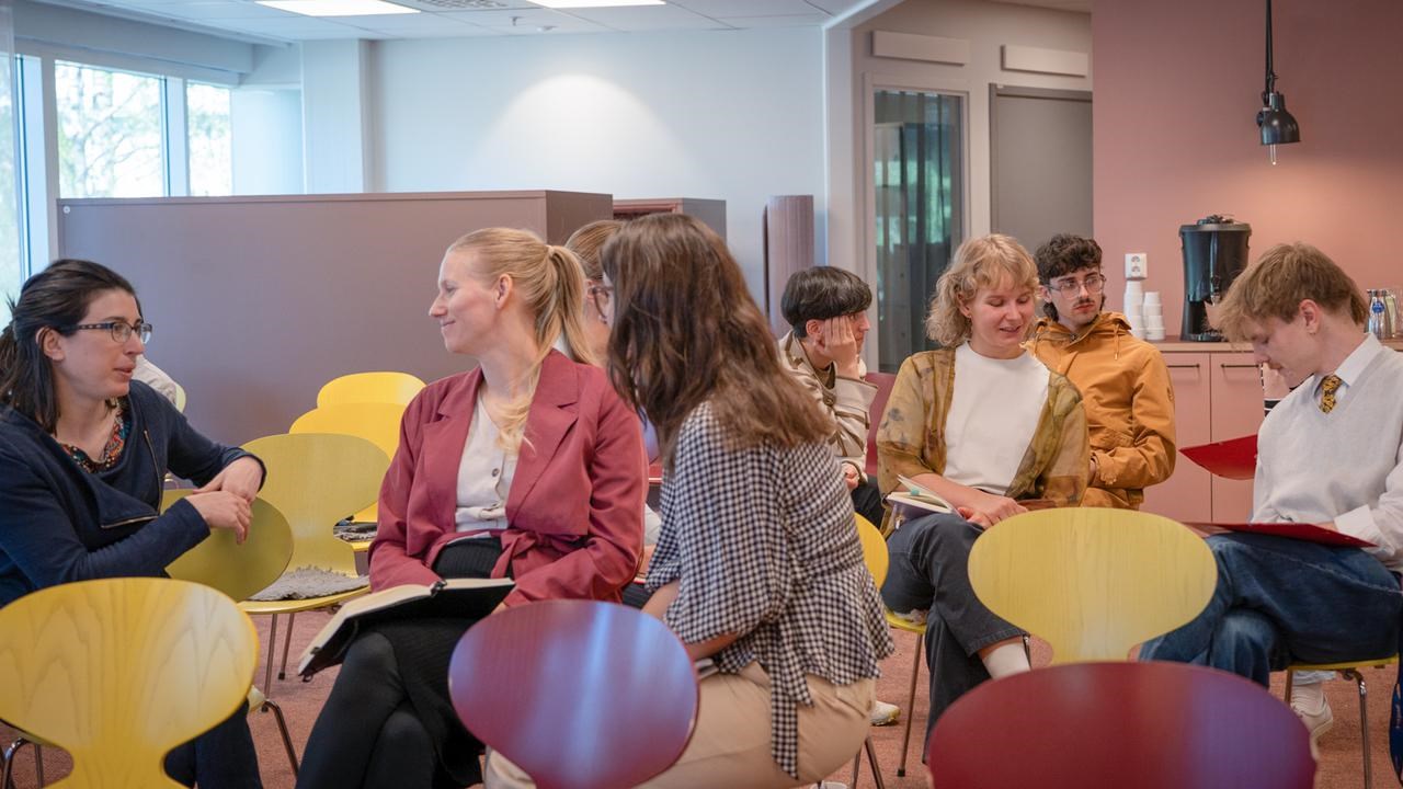 En grupp människor som sitter på stolar i ett rum och pratar.