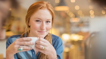 Rödhårig tjej dricker kaffe på ett café inomhus.