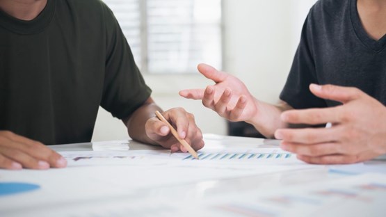 Detail of two people in conversation at a table with pen and paper.