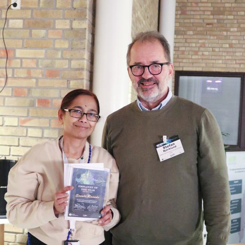 A woman holding an award and a man standing at the conference venue