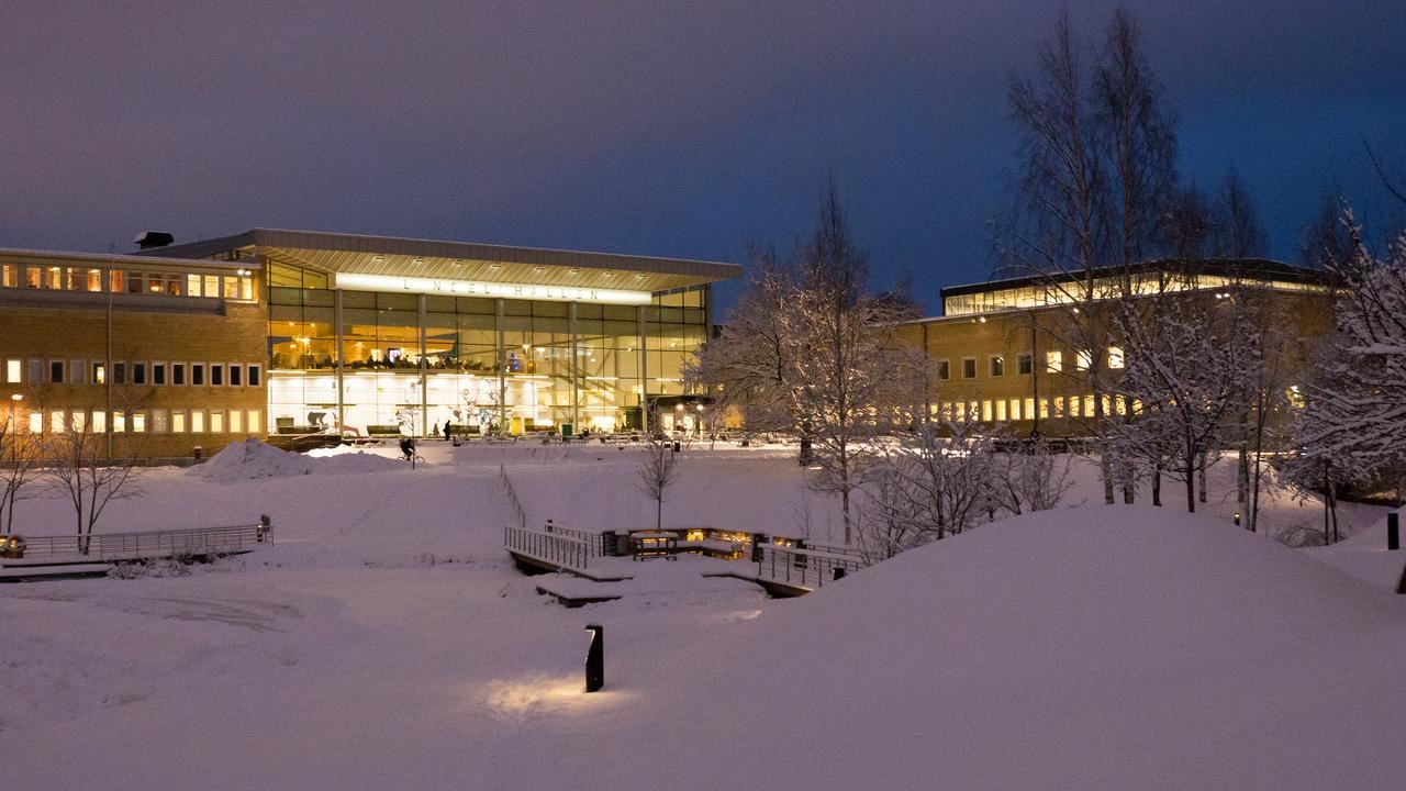 Vy över snötäckt Campus Umeå i skymningen i december.
