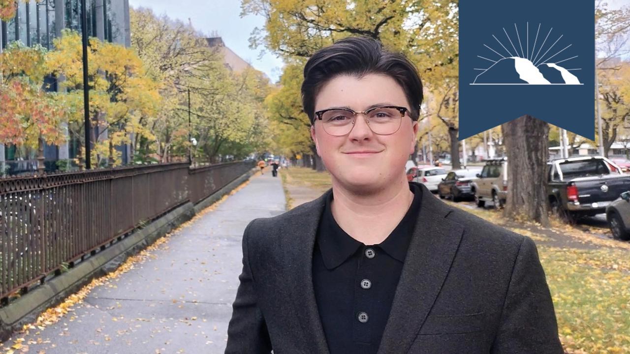 En man i kostym och glasögon står på en trottoar.