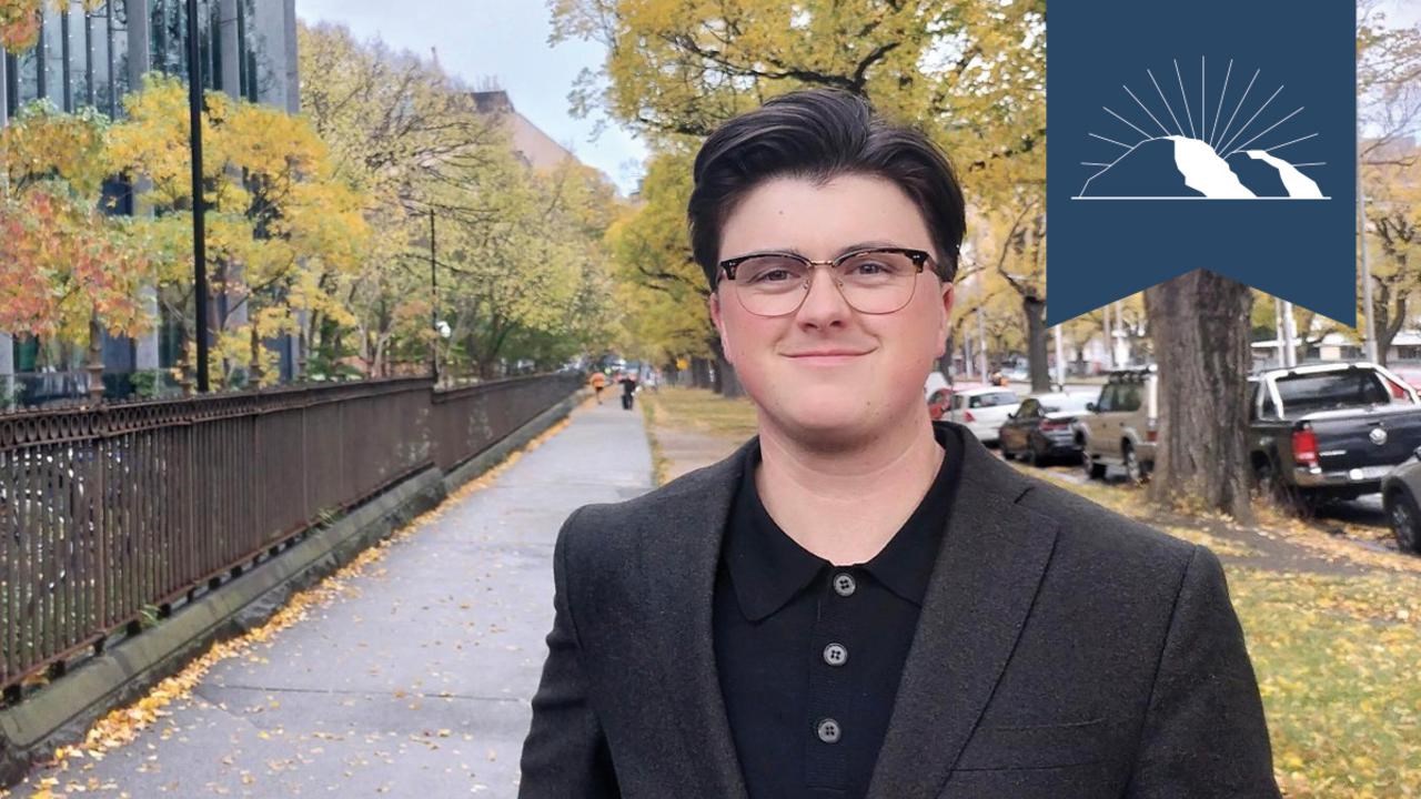 En man i kostym och glasögon står på en trottoar.