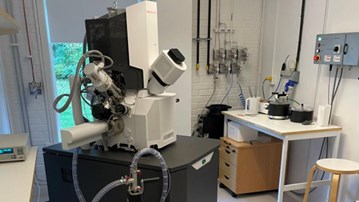 A large, 1x1x2 meter microscope. It is white and black, and connected with electric cables in a lab.