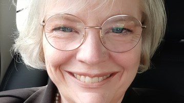 Porträttbild av Maria Nordin, som är glad med metallbågade glasögon och en kavaj/jacka på sig.