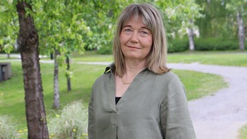 En kvinna står framför ett träd i en park.