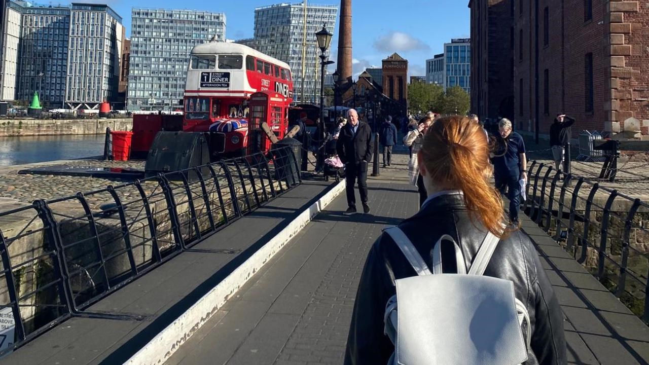 En kvinna med ryggs&auml;ck g&aring;r &ouml;ver en bro.